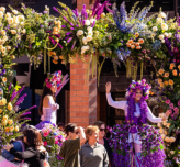 A photo of two people dressed in flower crowns dancing underneath a flower archway at the Tempe Blooms event.