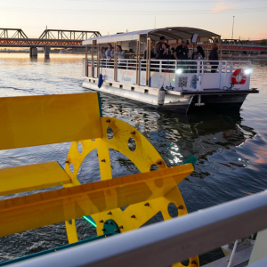 A pedal-powered boat full of people sails on Tempe Town Lake at sunset